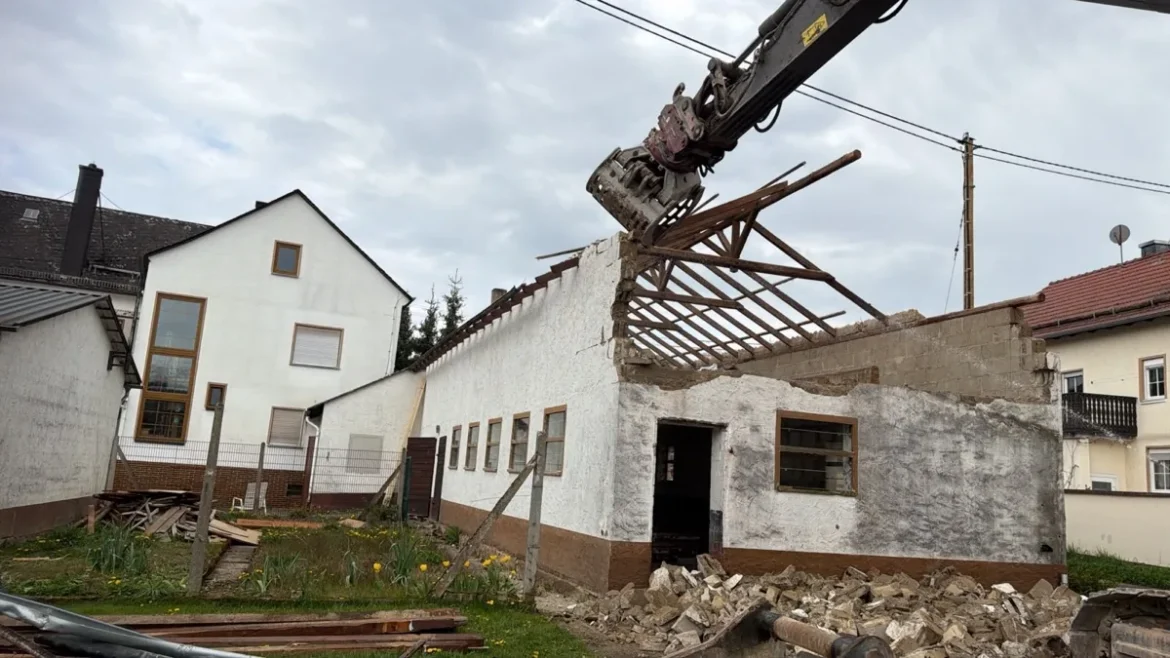 Bagger mit Sortiergreifer beim Abbruch eines eingeschossigen Nebengebäudes neben einem Wohnhaus