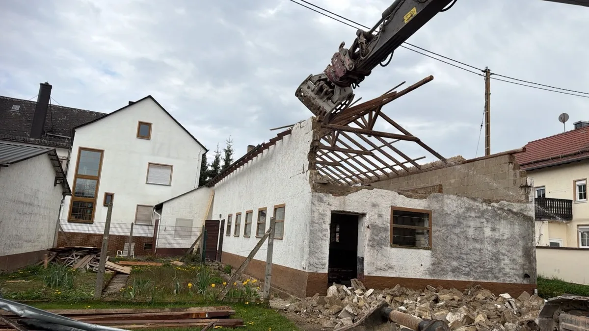 Bagger mit Sortiergreifer beim Abbruch eines eingeschossigen Nebengebäudes neben einem Wohnhaus