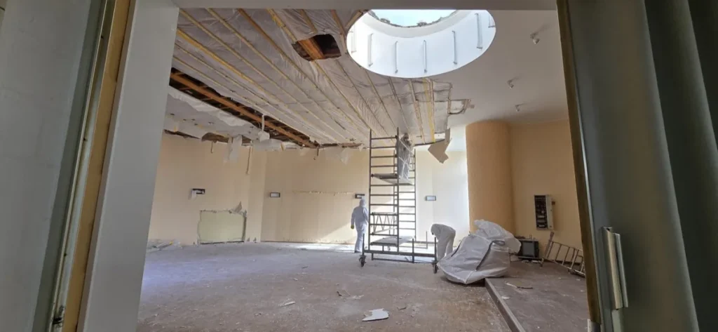Mitarbeiter in Schutzanzügen beim Rückbau einer abgehängten Decke, Deckenbereich mit Folie abgeschottet
