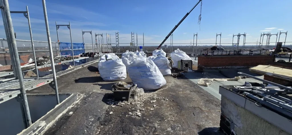 Eingerüstetes Flachdach mit Big Bags voller ausgebauter Dachbahnen und Bauschutt