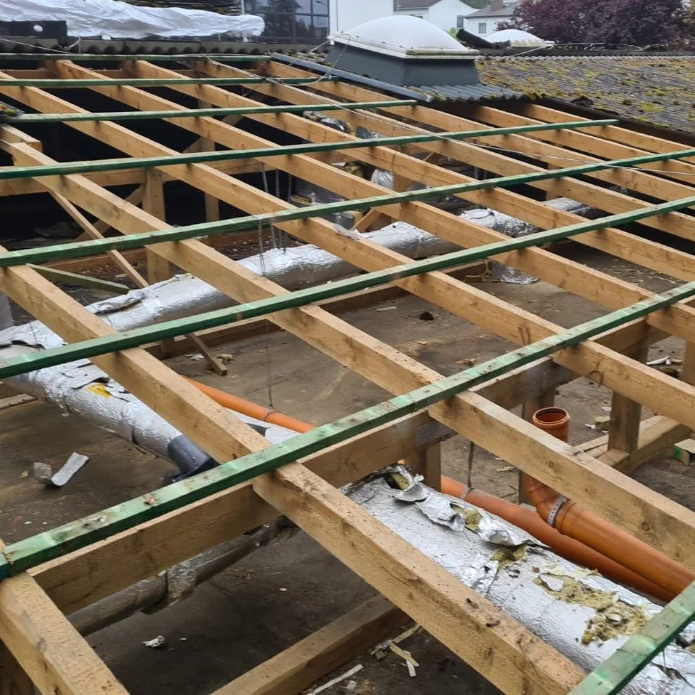 Freigelegte Holzkonstruktion eines Flachdachs mit gedämmten Lüftungsleitungen und Abwasserrohren