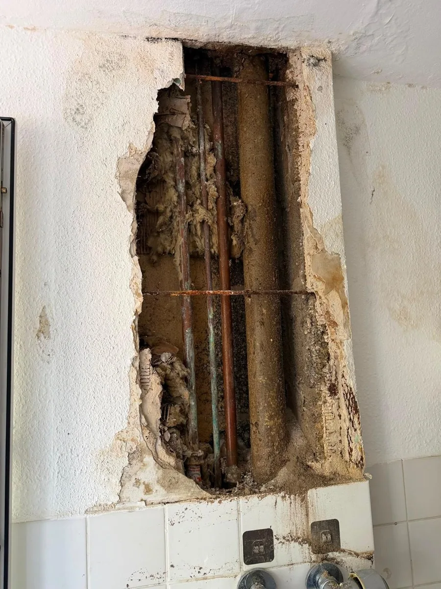 Geöffneter Installationsschacht mit alter Abflussleitung, Kupferrohren und Mineralwolldämmung